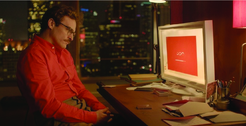 Fotograma de la película Her en el que Theodore, sentado frente a su ordenador en una habitación tenue, observa la interfaz roja del sistema operativo de IA con expresión melancólica