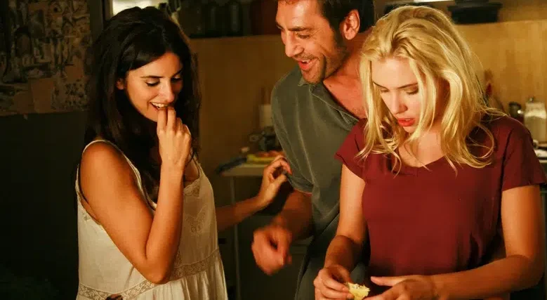 Tres personas jóvenes comparten un momento íntimo y distendido en una cocina, sonriendo y cocinando juntas, reflejando conexión y complicidad relacional.