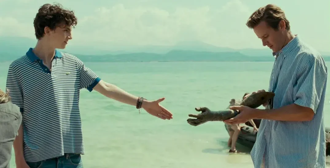 Escena íntima de dos hombres jóvenes en Call Me by Your Name, mirándose con complicidad y vulnerabilidad, evocando la dificultad y el valor de decir “te quiero”.